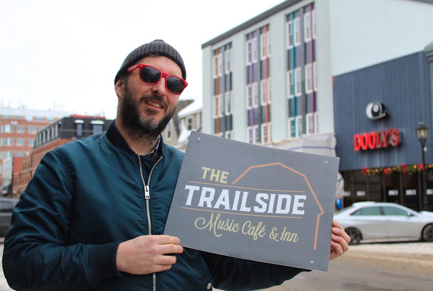 Pat Deighan holds an old business sign for The Trailside Music Café and Inn, which is moving out of Mount Stewart and into the tall, gray building behind him as Trailside Music Hall next year.