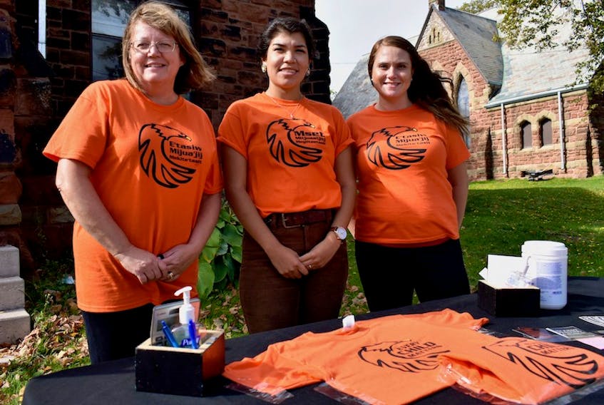 Yvette McKenna, left, Deidre Augustine and Brittany Lush, all of Mi'kmaq Printing and Design, stand behind the table in front of St. Paul's Anglican Church in Charlottetown, where they have been selling t-shirts for Orange Shirt Day Sept. 30.