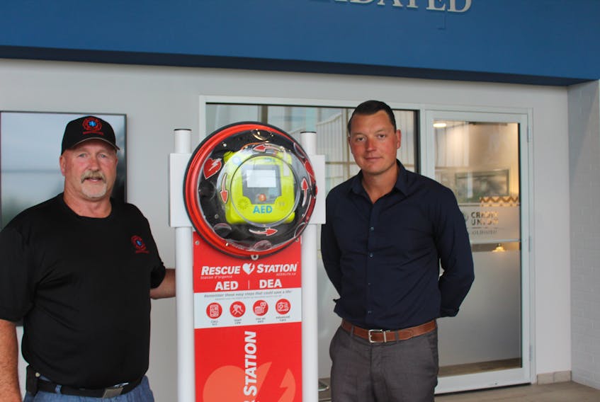 Miscouche firefighter John Mitchell and JP Desrosiers with the new defibrillator for the Credit Union Place's walking track.