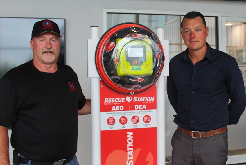 Miscouche firefighter John Mitchell and JP Desrosiers display the new defibrillator for the Credit Union Place's walking track.