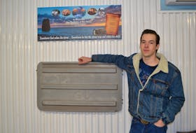 Tanner Gaudet stands beneath a memorial to Captain Glen DesRoches and first mate Moe Getson and beside the fishing tub lid he clung to during his hour-and-a-half struggle to make it to land last Sept. 18.