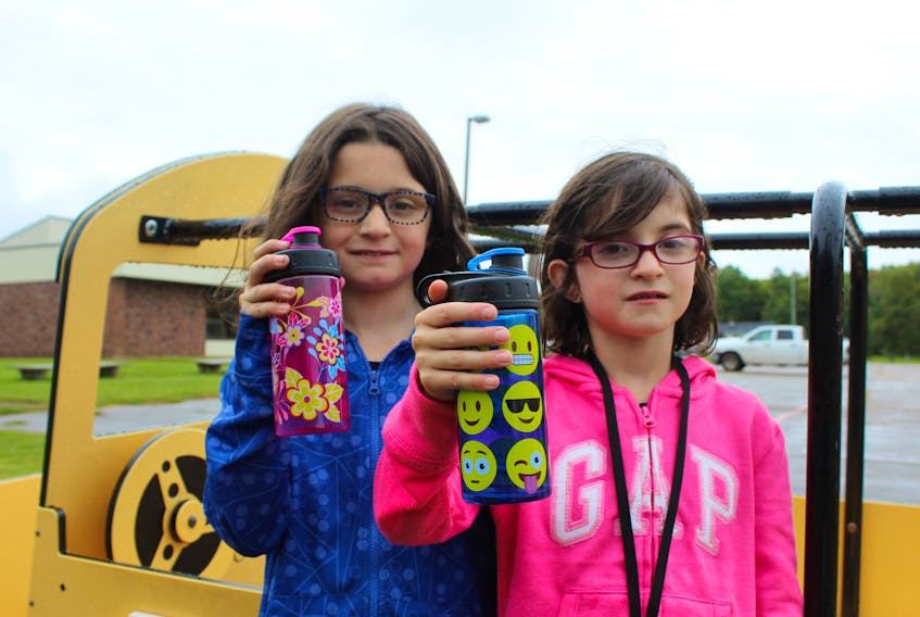 Liv, left, and Abi Bulman, show off their water bottles outside their school, Somerset Elementary School in Kinkora. Staff and students at the school will have to drink bottled water for a while, until Public School’s Branch finds a way to fix the ongoing water quality issues at the school.
