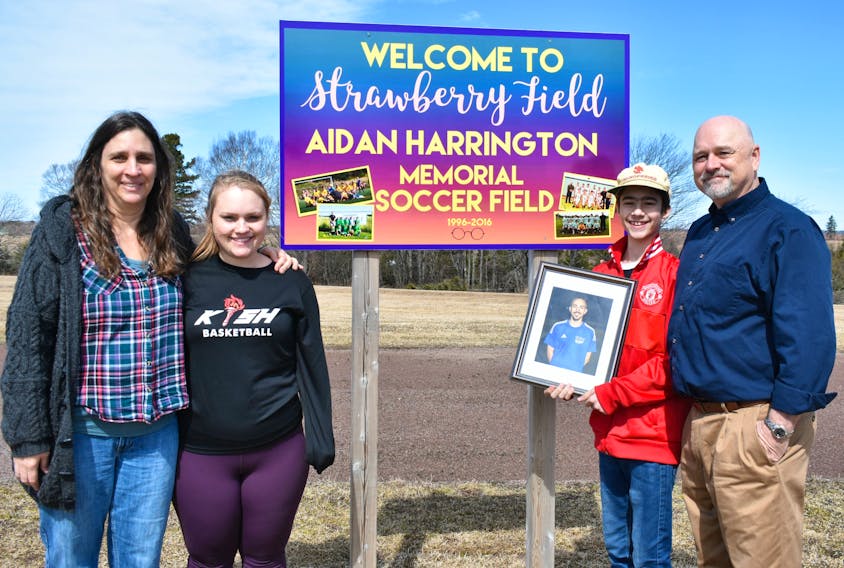Valerie Harrington, left, her daughter Hannah, son Quinn, and husband Alan stand in the field of Kensington Intermediate Senior High where Aidan coached soccer. A memorial sign for Aidan is planted in the background. The family hope to raise public awareness that all it takes is one bad decision when it comes to drugs.