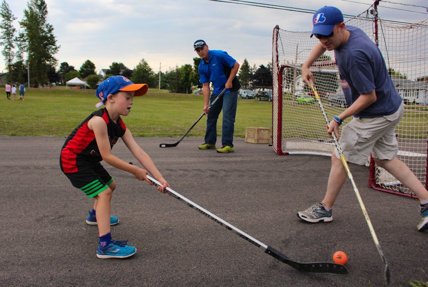 Dylan Thomas, 6, goes head to head with his father, Cory, as John Chaisson guards the net during a game of ball hockey at the recent block party arranged by the city to promote community spirit and develop bonds with neighbours.
