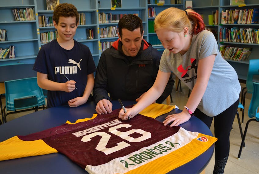 O’Leary Elementary School teacher Jonathon McAvinn and Grade 5 student Tasen Gallant look on as Olivia Dumville signs an O’Leary Hockeyville ’17 jersey. It’s part of a package, along with a $200 donation that the school is sending to the Humboldt Broncos.