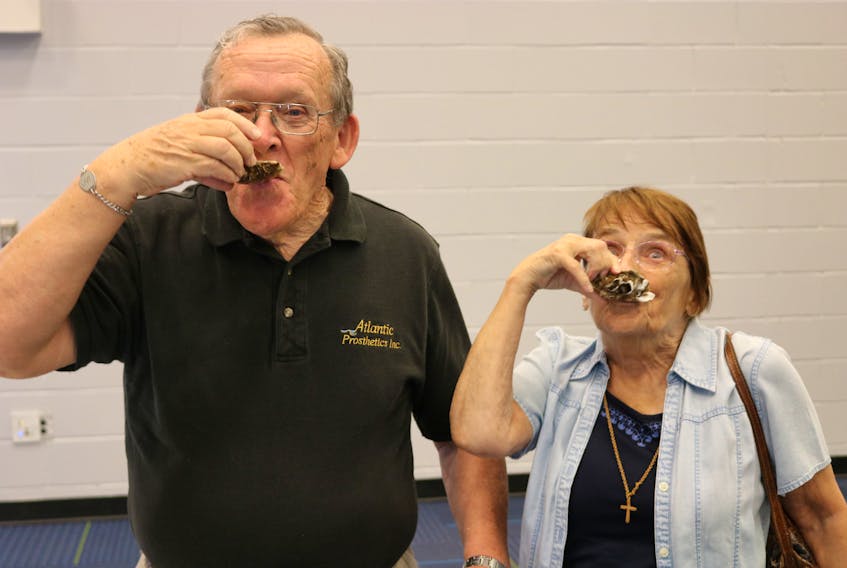 Father Eddie Cormier, left, and Marie Arsenault enjoy traditional Acadian treats at the recent announcement for the Congrès Mondial Acadien.