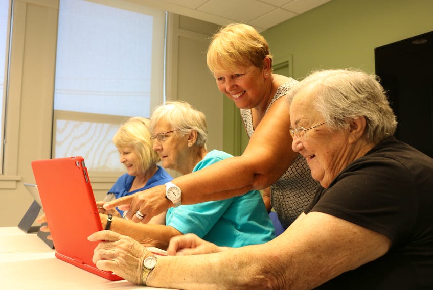 Jean Poirier, far left, Carolyn Taylor, second left, and Dorothy Farish, right, receive a technology lesson from EPSI Computer Club volunteer Shelley Lively (standing).