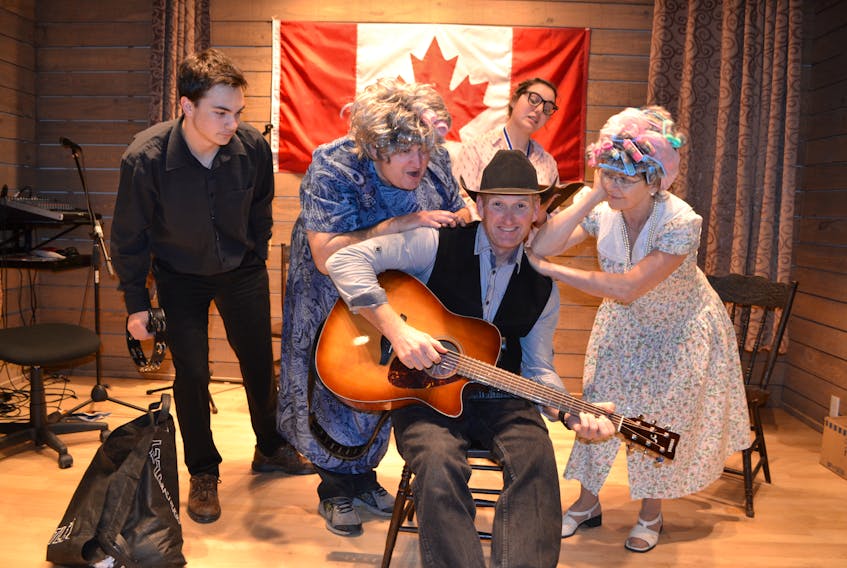 Stompin’ Tom (Chad Matthews) is fussed over by the Doyle sisters, Bernadine (Paul Shea), left, and Eileen (Helen LeClair).  Looking on are Hubie (Brayden McGuigan), a self-made cop, and Sam (Alyssa Harper), a journalism school graduate. They’re the cast of the Stompin’ Tom Centre’s new dinner theatre for 2018, ‘My Stompin’ Grounds – A Stomping Tom Story.’ It debuts July 2. The original show, ‘My Island Home – A Stompin’ Tom Story,’ returns June 19.