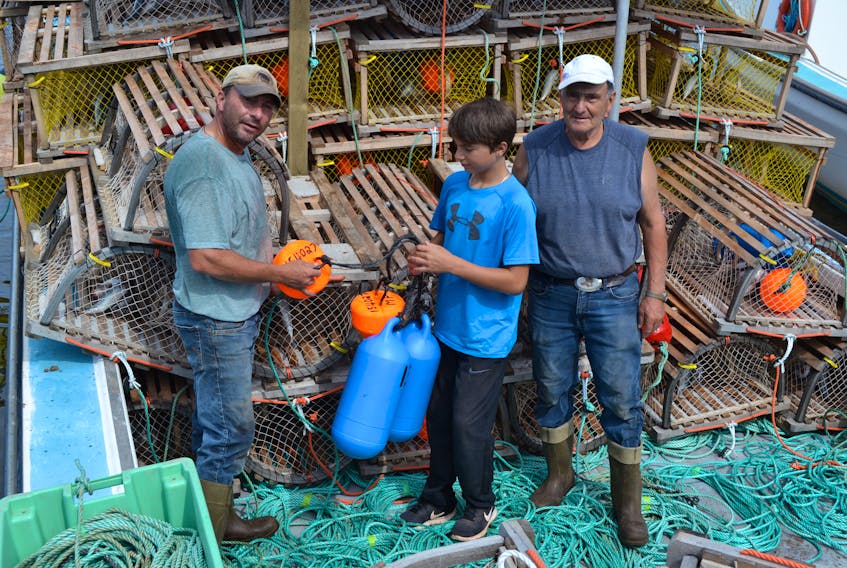 Three generations of the Perry family, from left, Ricky, Edmund and Captain Maurice Perry get ready at Skinners Pond Harbour on Wednesday for the Thursday morning start to their fall lobster fishing season. Their preparation included baiting traps and loading them onto their fishing boat, White Spray.