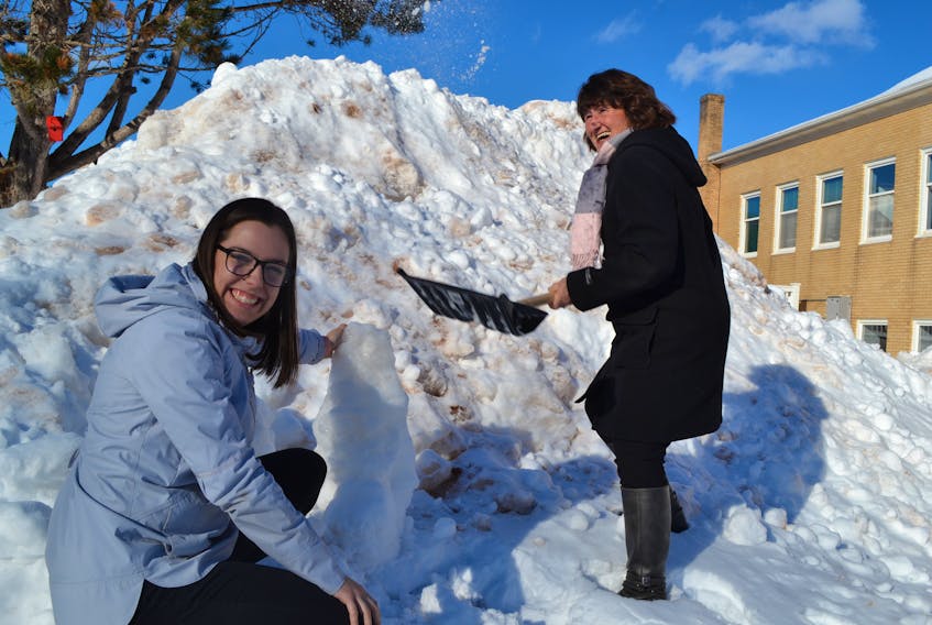 O’Leary Winter Carnival organizer Jessica Gillis, left, and town employee Faye MacWIlliams have fun in the snow while deliberating on a snow sculpture creation. There will be opportunities to build snow sculptures on February 16 during the Feb. 8 to 17 O’Leary Winter Carnival.