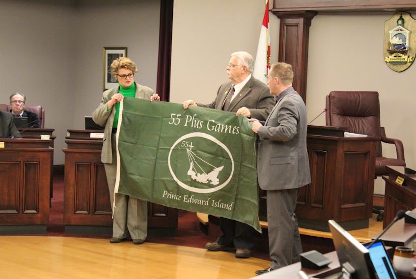Summerside Deputy-Mayor Norma McColeman, Mayor Basil Stewart and councillor Cory Snow unfurl the 55 Plus Games flag as McColeman announced the games will be hosted in Summerside in 2020 at the March 18 council meeting.