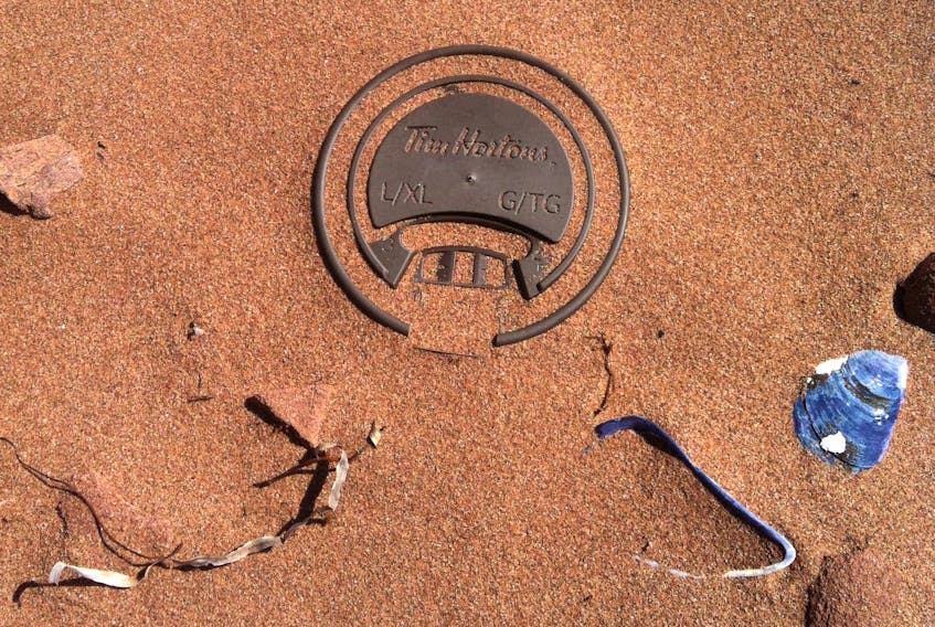 Plastic coffee cup lid embedded in P.E.I. beach.