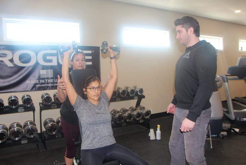 Liam Walsh, wellness centre lead, looks on as Chastity Morris spots Molly Peters cranking out a set of dumbbell shoulder presses.