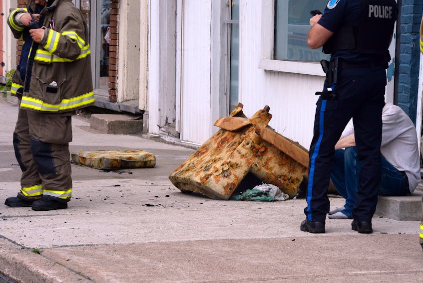 A Royal Newfoundland Constabulary officer checks his phone, while a firefighter gets ready to use his walkie-talkie and a resident sits on the step at the scene of a fire at a residence on Water Street in St. John’s Tuesday morning.
Firefighters made quick work of what has been termed a minor fire, although some furniture — including a chair — was damaged. —  Keith Gosse/The Telegram
