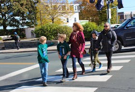 Bishop Feild parents and students cross one of the 12 crosswalks at Rawlins Cross on Saturday. During at least two crossings, vehicles pulled out into the road before the group had finished walking across the street. The brick building to the right in the background is the school.