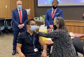 Dr. Jatin Morkar, clinical chief with the medicine program, receives the second COVID-19 vaccination for the province of Newfoundland and Labrador from Chief Medical Health Officer Dr. Jancie Fitzgerald as Premier Andrew Furey (background, right) and Health Minister John Haggie look on. — Keith Gosse The Telegram