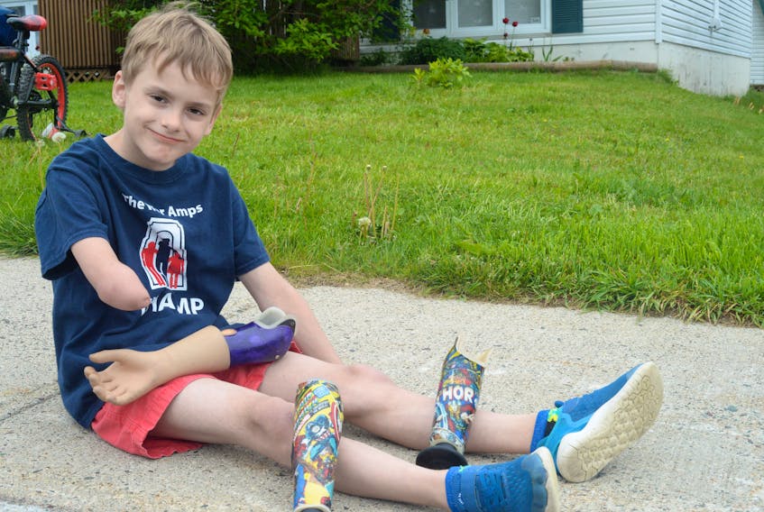 Kirill Facey sat on the sidewalk in front of his home showing some of his specialized “amputee arms.” One of his arms is decorated with Spider-Man and Captain America.
