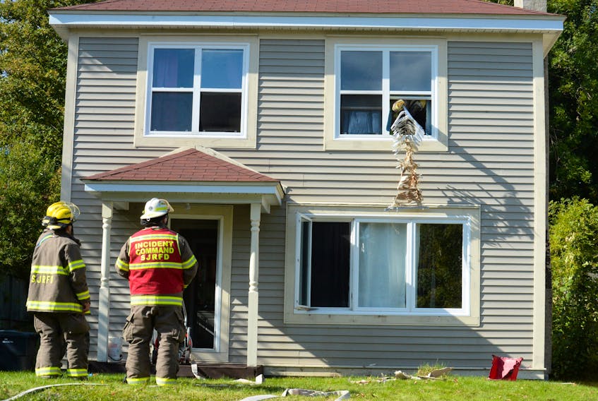 Firefighter Mike Newhook tosses a scorched set of window blinds to the ground from the bedroom where a house fire originated Wednesday on Guy Street in St. John’s, as firefighters Steve Hyde and Justin Chow and Capt. Craig Cox look on.