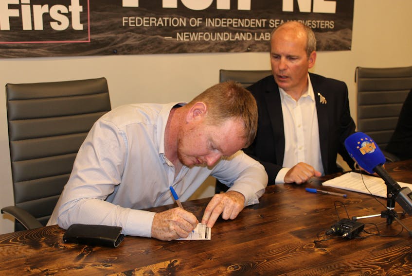 FISH-NL secretary/treasurer Jason Sullivan signs his membership card during a news conference Monday at FISH-NL's offices in St. John’s, while FISH-NL president Ryan Cleary looks on.