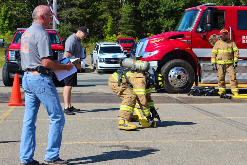 Two members of the Cape Breton Regional Fire Service, Gilbert MacIntyre, left, and Dave Witzell watch as Luke Einish of Team Quebec rolls up a fire hose during the Aboriginal Firefighters Association's national competition hosted this weekend in Eskasoni.