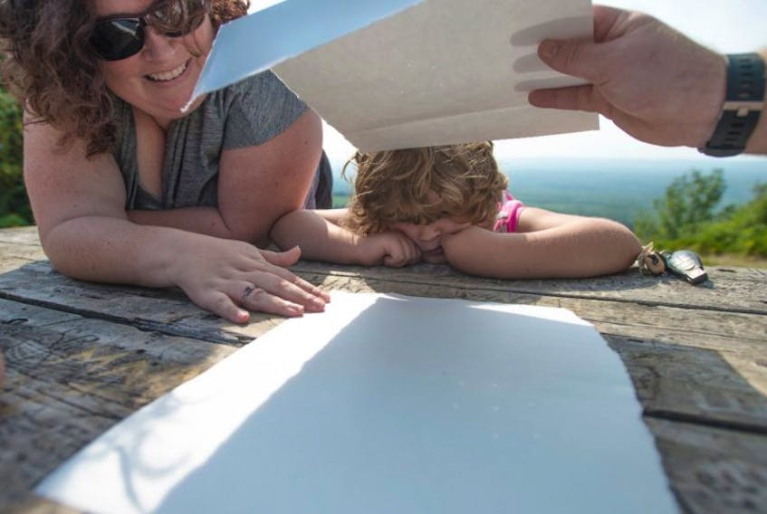 Karen Hotson and her daughter Lily watch Monday’s Solar Eclipse through pin holes in bristol board at the Greenhill Look off.  ( Mark Goudge/SaltWire)
