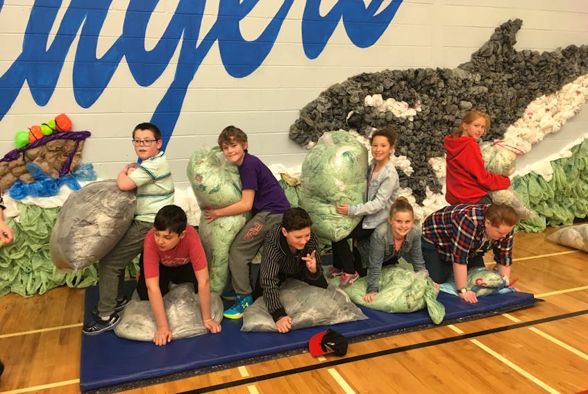 Members of the Spring Street Academy Sustainability Squad stand and kneel in front of the mural on the wall of the gymnasium. Students at the school collected more than 20,000 plastic bags – many of which were created into a temporary mural depicting a marine scene.