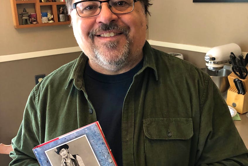 Charlie Rhindress stands with a copy of his biography of Stompin’ Tom Connors: The Myth and The Man. He is hosting a series of streaming interviews with people who worked with or knew Stompin’ Tom.