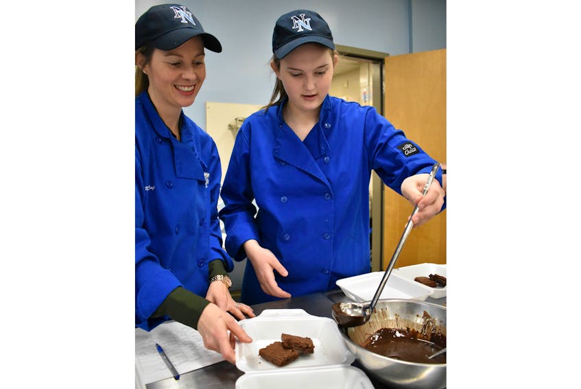 Grade 11 student Megan James (R) helps her teacher Rachael Kinch pour chocolate sauce on brownies Friday at North Nova Education Institute. Sixteen students cooked lunch for their families as part of their Career Exploration Program’s culinary arts field.