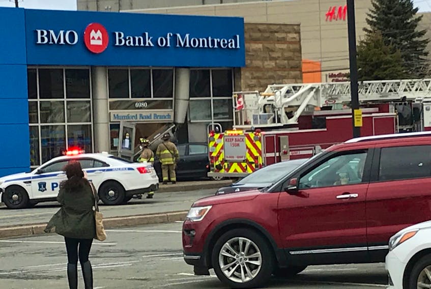 Emergency workers attend the scene of a collision at the Mumford Road branch of the Bank of Montreal on Friday. Police confirm that the car was not driven intentionally into the entrance of the bank, and a 25-year-old man has been charged with multiple infractions, including texting while driving.