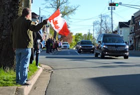 A spectator waves a Canadian flag as Captain Jennifer Casey's motorcade proceeds along Almon Street, just past her family’s home, on Sunday.