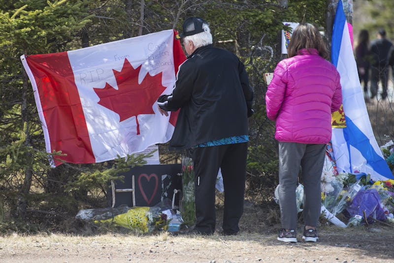 Garry Rogers and his wife Stella place a Canadian flag at a memorial at the end of Portapique Beach Road on Wednesday, April 22, 2020. Rogers lives in Truro but is originally from Cape Breton. He wanted to place the flag on behalf of the people of Cape Breton who can’t come in person to express their condolences. - Ryan Taplin