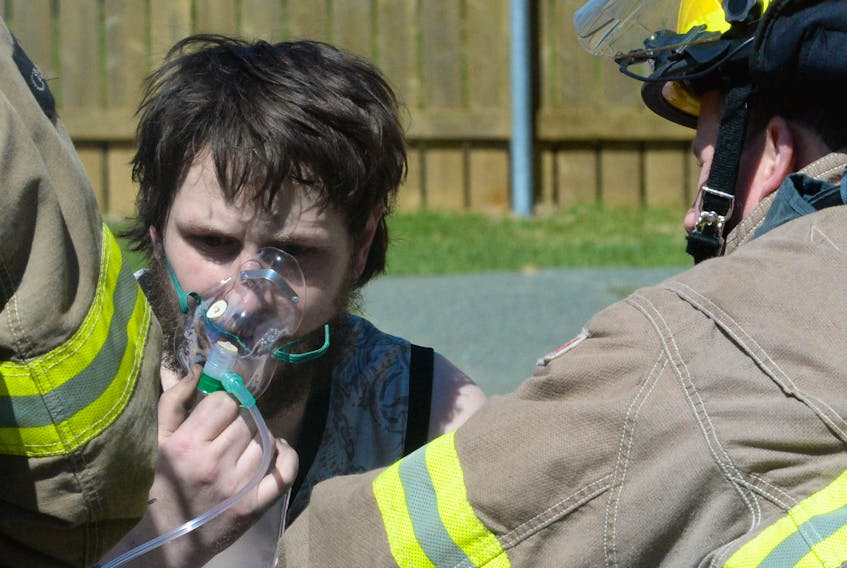 Firefighter Dave Wheeler assists a male resident with oxygen as they await the arrival of Eastern Health paramedics Wednesday afternoon during a fire at Wigmore Court in St. John’s.