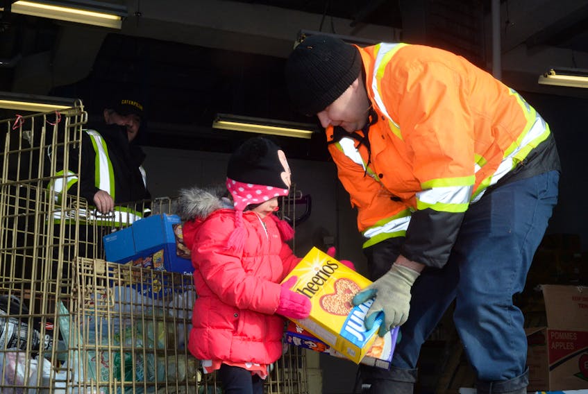 Allison Clark, 3, helps Community Food Sharing Association employee Dwayne King place bags of food into the storage cage Monday at the associations new location on Pippy Place.