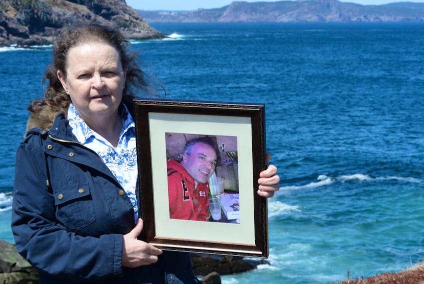 Daphne Walsh stands at Cape Spear on Monday afternoon with a framed photo of Keith Walsh Sr., one of the four fishermen from Shea Heights who were lost at sea on Sept. 6, 2016 just off Cape Spear.
