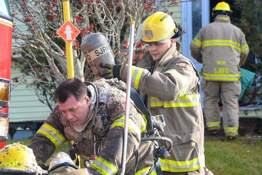 Covered in insulation particles from battling a fire inside a burning house, firefighter Darrell Pennell (front) gets his breathing apparatus changed with assistance from fellow firefighter Matt Mercer before heading back into the home. — Joe Gibbons/The Telegram
