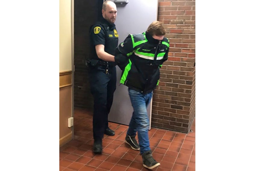 Lucas Dawe, 20, hides his head under his jacket as sheriffs escort him into a St. John's courtroom Thursday morning.