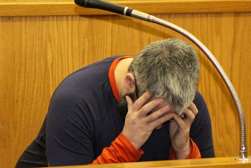 David Snow, 36, hides his face from media cameras as he sits in the dock at Newfoundland and Labrador Supreme Court in St. John’s Tuesday afternoon. He has pleaded guilty to more than a dozen child sex offences involving five young girls, including sexually assaulting two of them and making peepholes in bathroom walls in order to secretly record them.