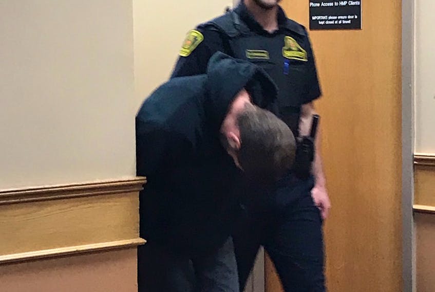 Raymond Trudel, 35, hides his face from reporters as he is escorted out of a provincial courtroom in St. John's Wednesday afternoon. Trudel is facing more than 50 charges related to an alleged rental scam.
