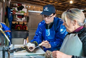Kimberly Orren (right), co-founder and project manager of Island Rooms of Petty Harbour Fishing for Success, shows a member of the Choices for Youth Mama Moments program how to remove the meat from a cod after it has been filleted.