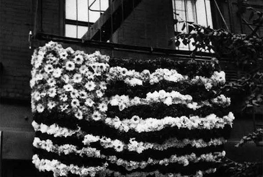 A flag of flowers hangs from a fire escape in New York city in the days following the 9-11 attacks. “The candles and flags and vases of flowers on sidewalks throughout the city were spontaneous messages from anonymous strangers trying to communicate with each another. A visual dialogue in a way,” Magi Dominc writes. “The vases of flowers outside fire houses spoke for themselves.” — Photo courtesy Magie Dominic
