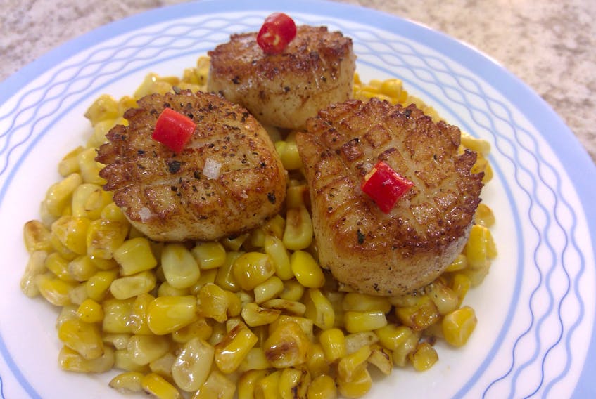 Scallops seared in brown butter sit on a bed of sweet corn.