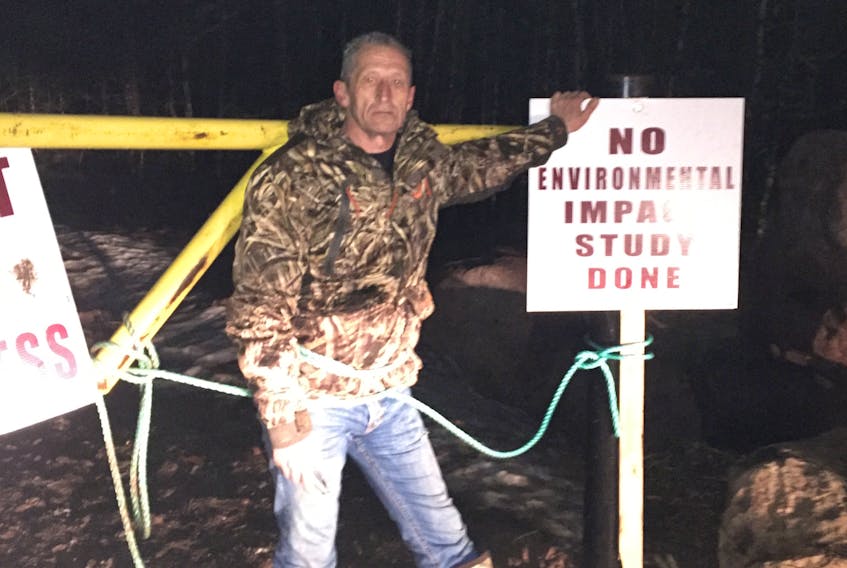 Mike Cooze tied himself to a gate at the Big Triangle Pond Mineral Exploration Access Road entrance in protest of the road being built without a full Environmental Impact Statement, and in protest of potential future gold mining operations in the area.