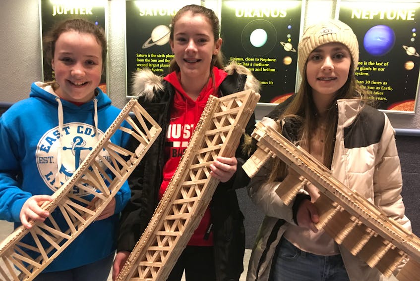 Selena Ryan, Grace Hemeon, and Olivia Taylor show off the bridges they built using only popsicle sticks and white glue.