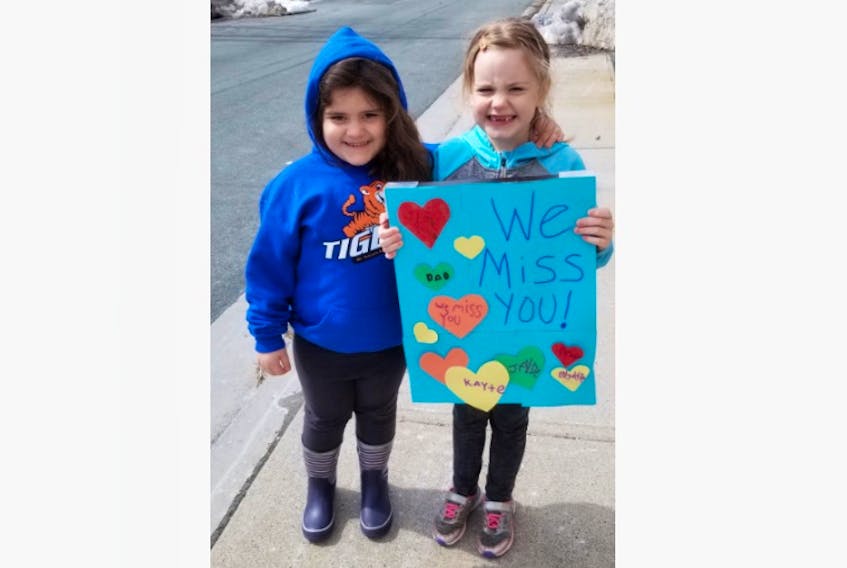 Kayte, 5, and Jayde Phillips, 7, hold a sign for their teachers to see during Monday’s motorcade of St. Teresa’s School staff.