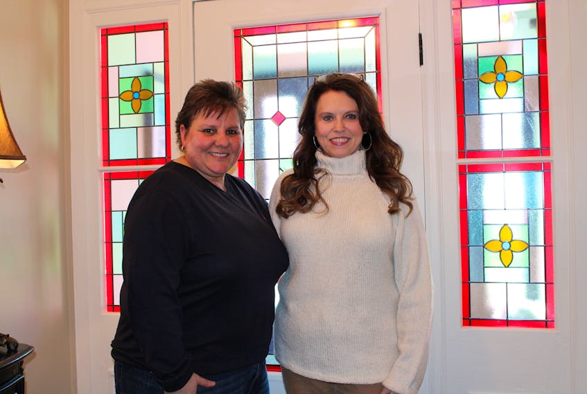 Lori Rogers and Roxanne Cullen Przybysz stand in front of the stained glass transom window in the front entrance to their home.