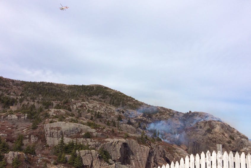 A Forestry chopper flies over smoke on a hill in Quidi Vidi Village on Tuesday.