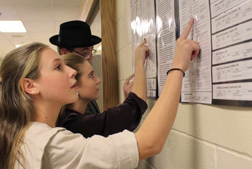Ava Schurman, left, Hailey Birch and Kayden Desroche look for their identities on the list of survivors and deceased from the Halifax Explosion. The three, along with other SIS students and staff, were given identities of real people who lived in Halifax at the time of the explosion 100 years ago.