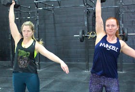 Katrina Hutchinson, left, and Colleen Schurman complete dumbbell clean and jerks, one of the exercises in the open's 18.1 workout.