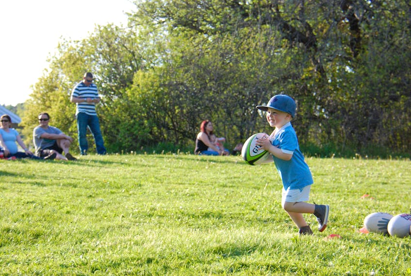 Three-year-old Bennett Ellis of Stratford smiles as he runs with the rugby ball at the Co-op Field in Queen Elizabeth Park in Charlottetown on June 1 during free Try Rookie Rugby session.