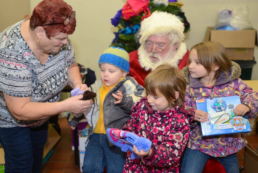 Betty Begg and Santa surprise siblings, from left, Nathaniel, Elizabeth and Lori Chiasson, with some new mitts and toys during the recent Christmas Care Fair held at the P.E.I. Farm Centre. The fair provided families and individuals with just about anything they would need from food and clothes to books and toilet paper.